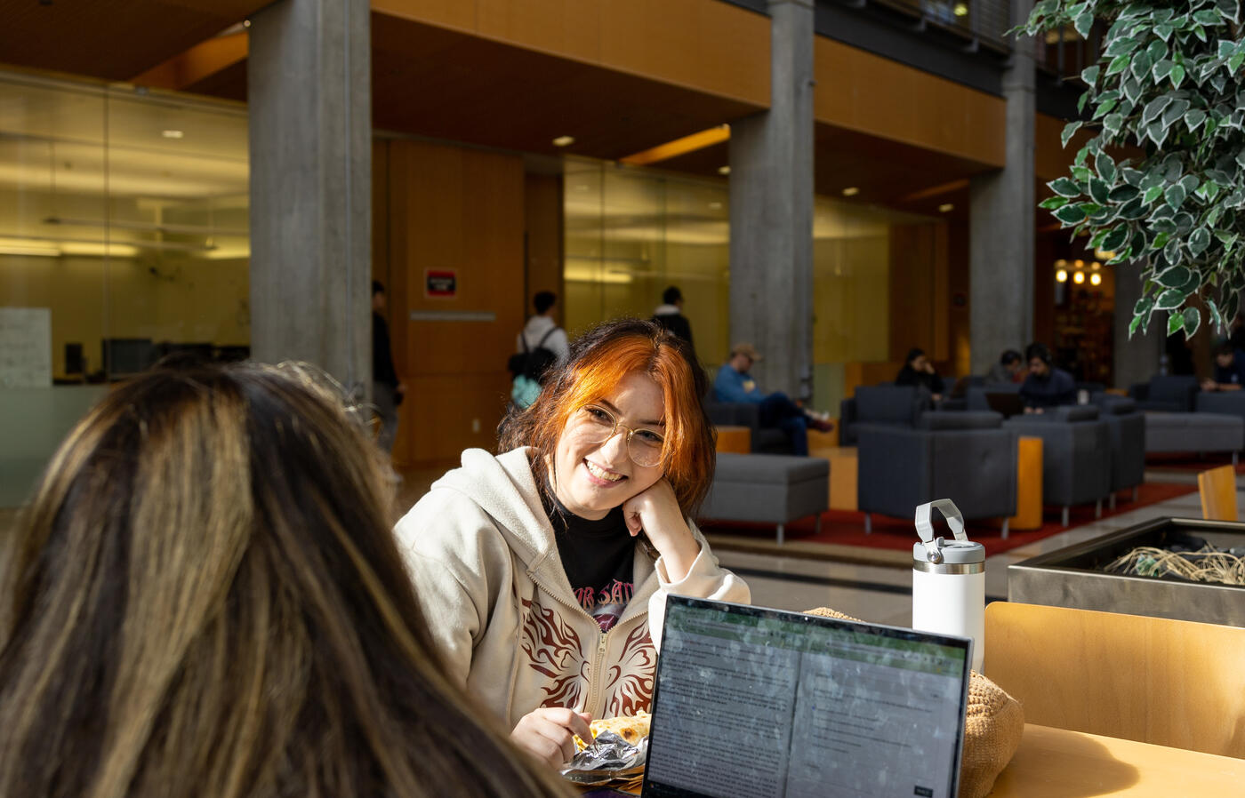 Two female students sharing a table and chatting in a college building common area