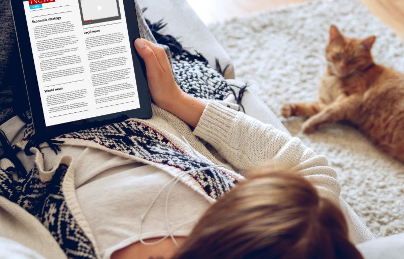 A young woman sitting on the floor reading the news on a tablet with a cat laying next to her