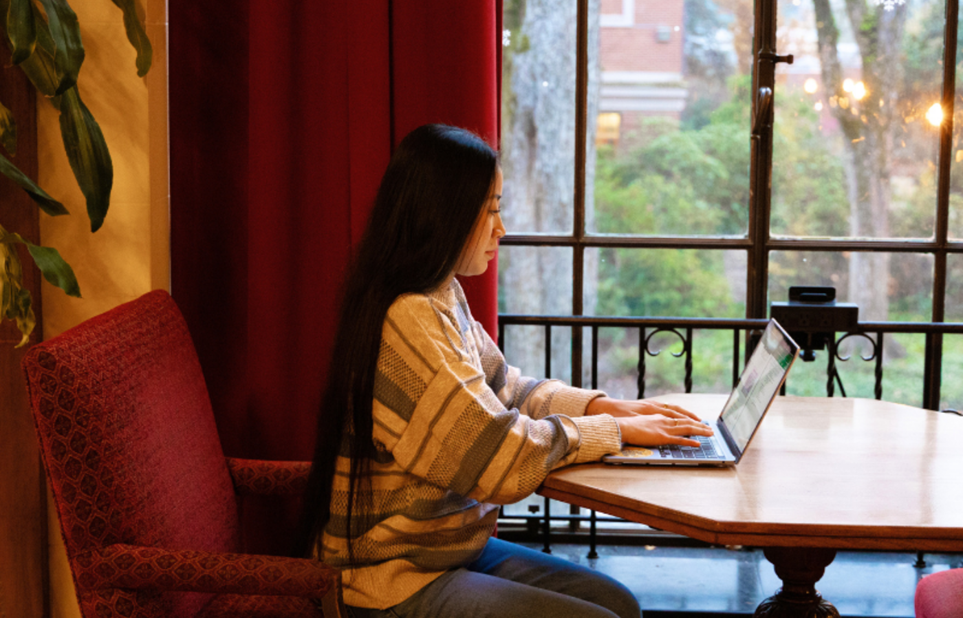 College student working on laptop at a table next to a window at the Memorial Union