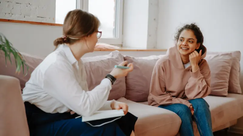Young adult female sitting on couch talking with mental health therapist