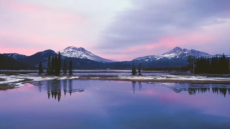 Pink and purple clouds reflecting on an Oregon lake with snow topped mountains in background
