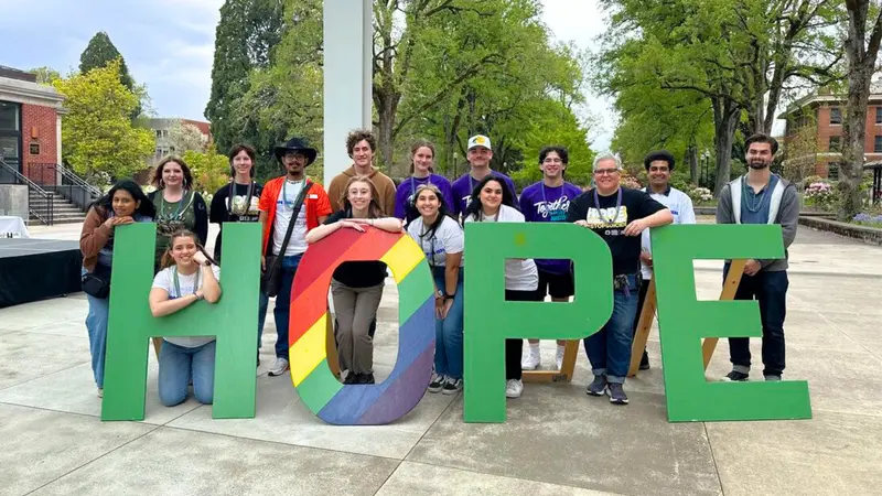 Student staff and volunteers at a campus event posing in front of a large sign reading "HOPE"