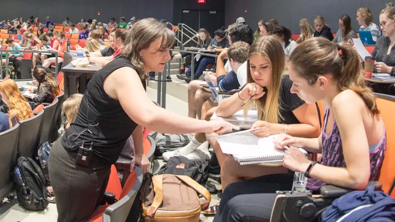 Instructor assisting two students with coursework in a large lecture hall