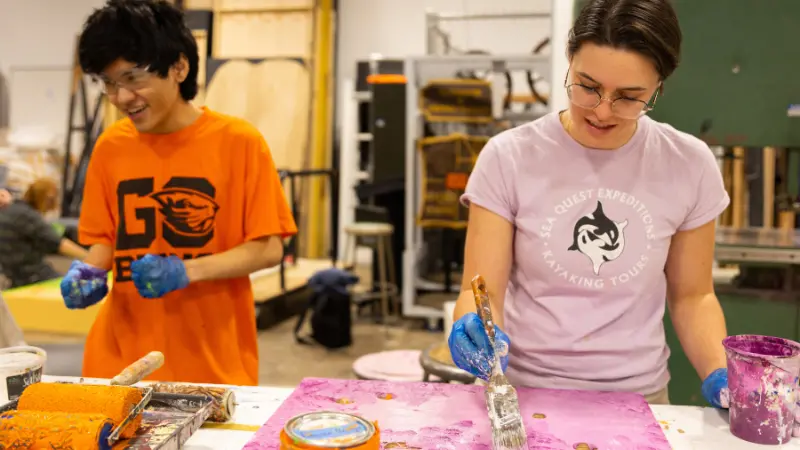 Two students standing next to one another while working on art projects in class