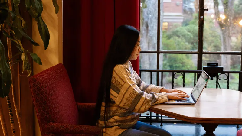 A student sitting at a table in MU Lounge working on a laptop