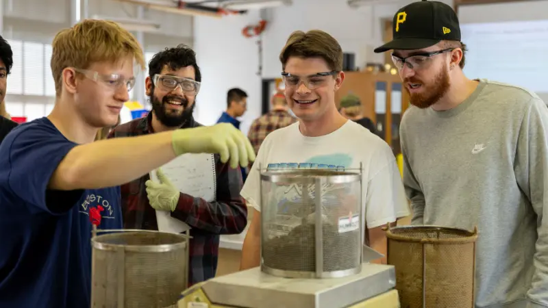 Three students and an instructor, all wearing goggles, looking at a student project
