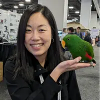 Dr. Lilian Wong posing with a green parrot sitting on the palm of her hand