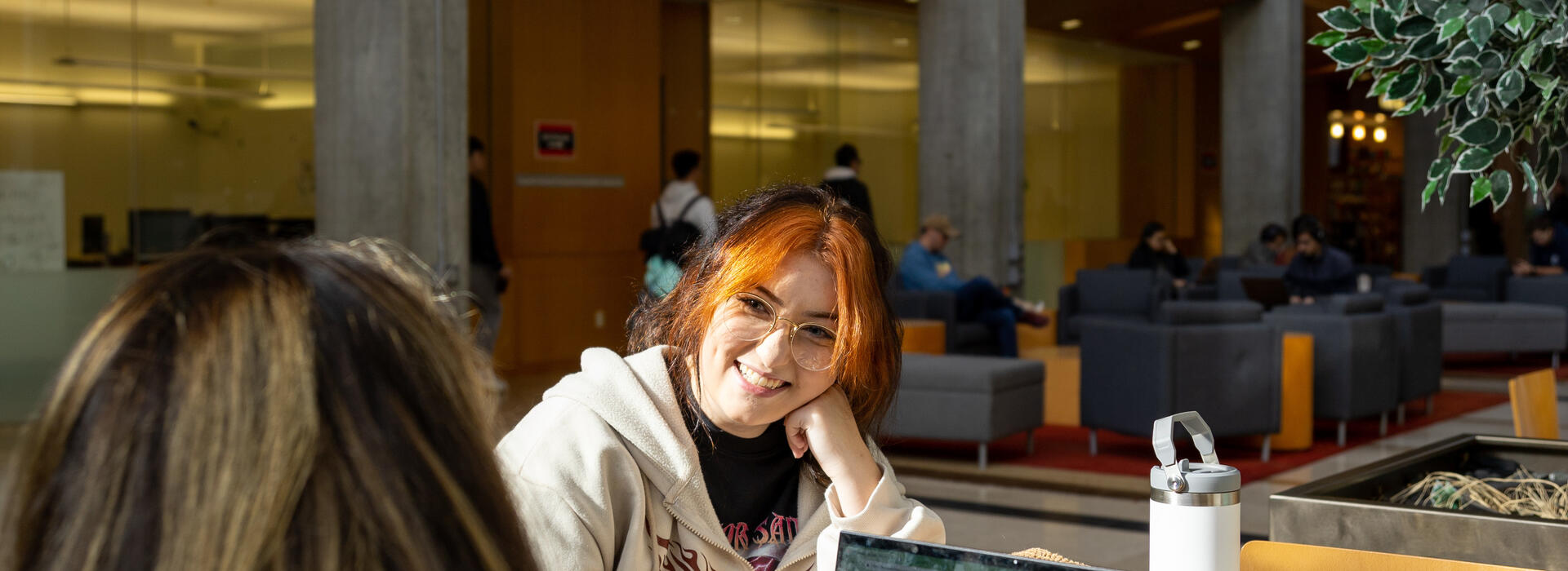 Two female students sharing a table and chatting in a college building common area