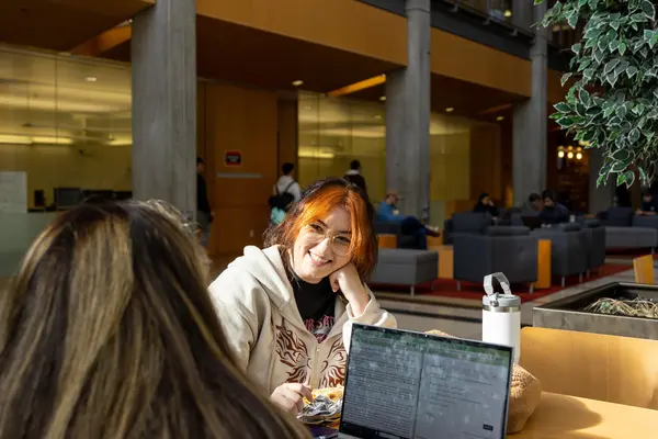 Two female students sharing a table and chatting in a college building common area